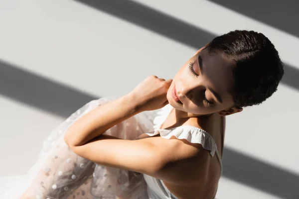 Visão aérea de bailarina bonita sentada em fundo cinza com luz solar e sombra — Fotografia de Stock