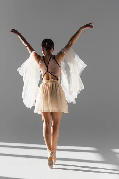 Vue arrière de la ballerine dansant avec tissu sur fond gris avec lumière du soleil — Photo de stock