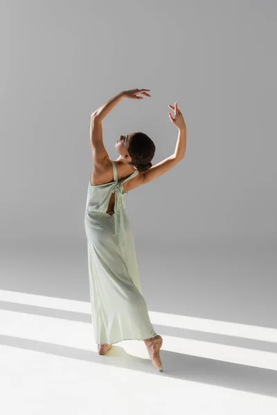 Вид збоку молодої танцівниці в взутті, що стоїть на сірому фоні з сонячним світлом — стокове фото