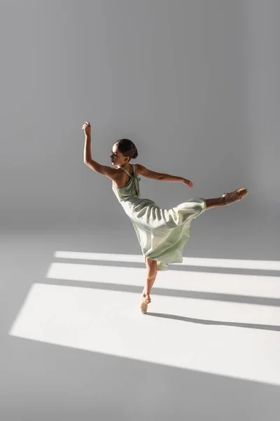 Bailarina dançando e de pé em uma perna sobre fundo cinza com luz solar — Fotografia de Stock