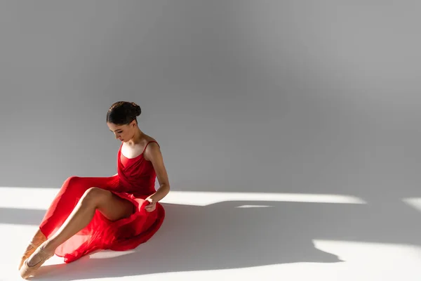 Danseuse classique regardant robe rouge sur fond gris avec lumière du soleil — Photo de stock