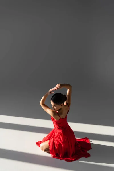 Pretty dancer in red dress posing on grey background with sunlight — Stock Photo