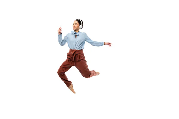 Bailarina sonriente en auriculares usando smartphone mientras salta aislada en blanco - foto de stock