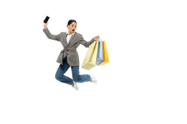 Дивовижна жінка зі смартфоном тримає сумки і стрибає ізольовано на білому — стокове фото