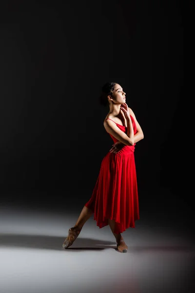 Side view of classical dancer in pointe shoes standing on black background — Stock Photo