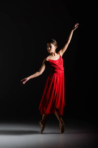 Балерина в красном платье танцует на черном фоне — стоковое фото