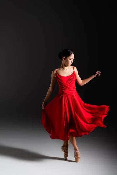 Молода брюнетка балерина в червоній сукні танцює на чорному тлі — стокове фото