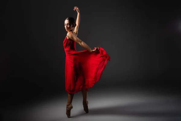 Bastante bailarina segurando vestido vermelho enquanto dança no fundo preto — Fotografia de Stock