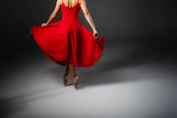 Cropped view of ballerina in red dress dancing on black background — Stock Photo