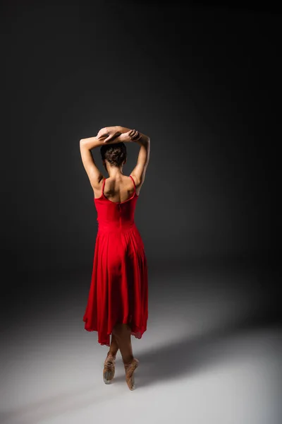 Back view of ballerina in red dress and pointe shoes standing on black background — Stock Photo