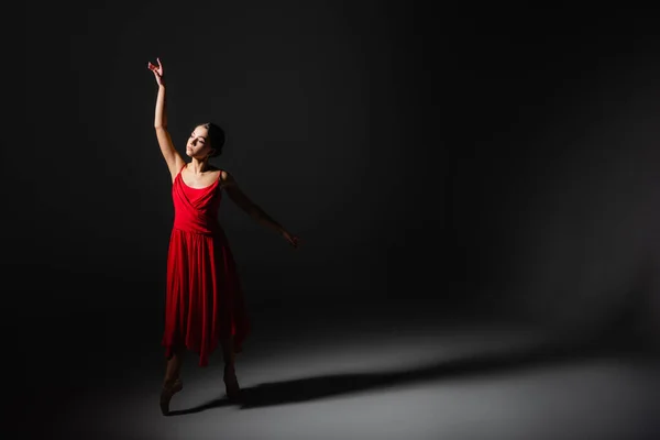 Ballerina in red dress dancing in light on black background — Stock Photo