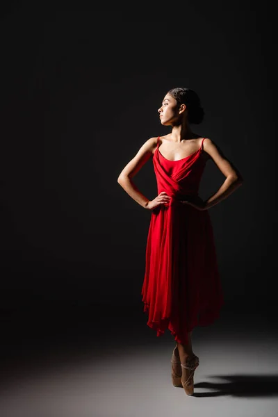 Side view of ballerina holding hands on hips in light on black background — Stock Photo