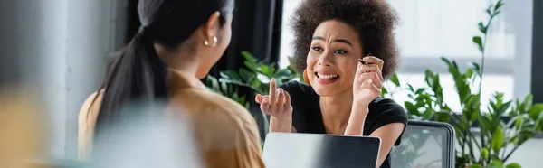 Donna d'affari afro-americana eccitata che punta il dito mentre parla con un collega sfocato, striscione — Foto stock