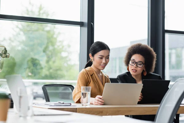 Jóvenes mujeres de negocios interracial que trabajan cerca del ordenador portátil en la oficina - foto de stock