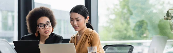 Asiático e africano americano gestores olhando para laptop enquanto trabalhava no escritório, banner — Fotografia de Stock