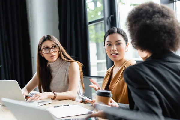 Mulher asiática gesticulando enquanto conversa com parceiros de negócios multiétnicos no local de trabalho — Fotografia de Stock