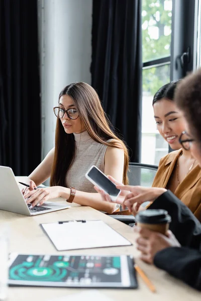 Borrosa africana americana mujer de negocios apuntando a smartphone en manos de asiático colega — Stock Photo