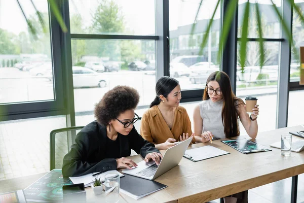 Afro-americana empresária digitando no laptop perto de colegas inter-raciais que trabalham com documentos — Fotografia de Stock