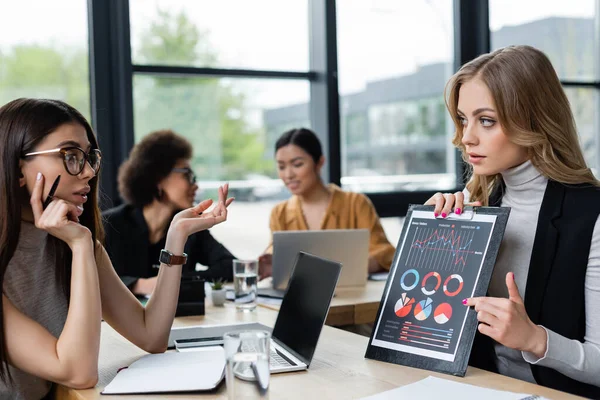 Blonde businesswoman showing analytics to colleague near blurred managers — Stock Photo