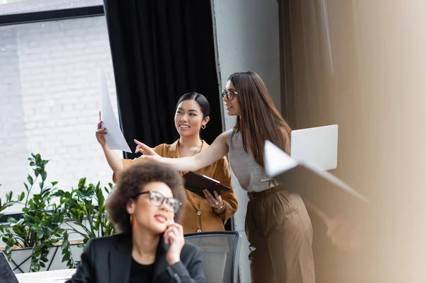 Partner commerciali interrazziali che lavorano con documenti vicino alla donna afroamericana offuscata che parla sul cellulare — Stock Photo