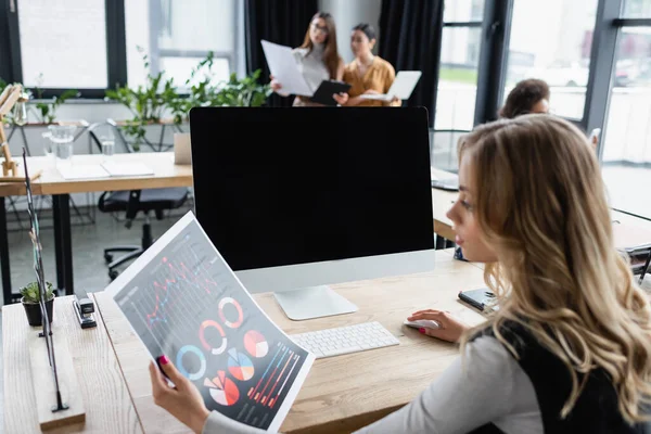 Gestionnaire flou en regardant les graphiques près du moniteur et des partenaires commerciaux sur fond — Photo de stock