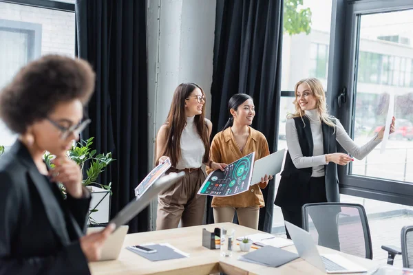 Verschwommene afrikanisch-amerikanische Geschäftsfrau in der Nähe multikultureller Manager, die mit Analysen im Hintergrund arbeiten — Stockfoto