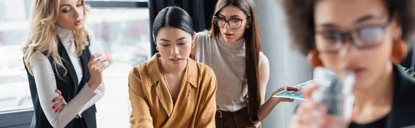 Donne d'affari multietniche che lavorano in ufficio vicino a un collega afroamericano offuscato, striscione — Foto stock