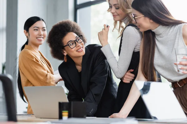 African american businesswoman smiling near multiethnic colleagues near laptop in office — Stock Photo