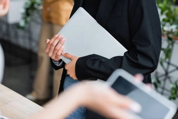 Vue recadrée d'une femme d'affaires tenant un ordinateur portable près d'une tablette numérique au premier plan flou — Photo de stock