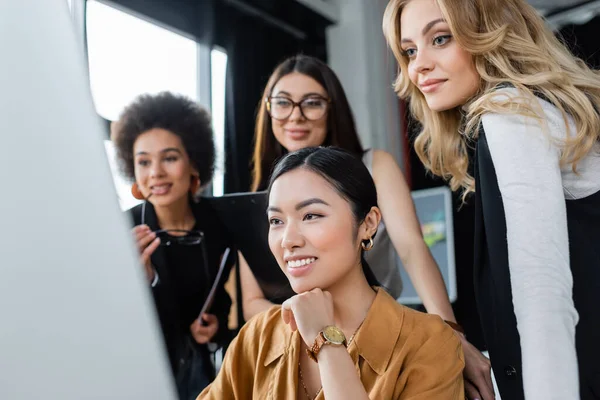 Heureuses femmes d'affaires multiethniques regardant l'écran d'ordinateur flou dans le bureau — Photo de stock