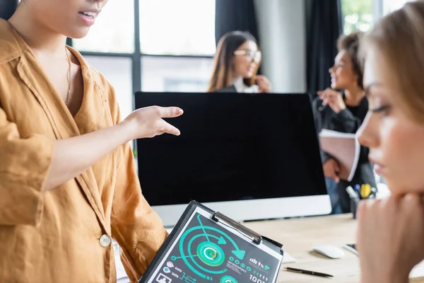 Gerente apontando para monitor com tela em branco perto de infográficos e colega borrado — Fotografia de Stock