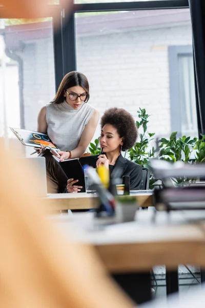 Brunette femme d'affaires pointant du doigt un ordinateur portable entre les mains d'un collègue afro-américain — Photo de stock