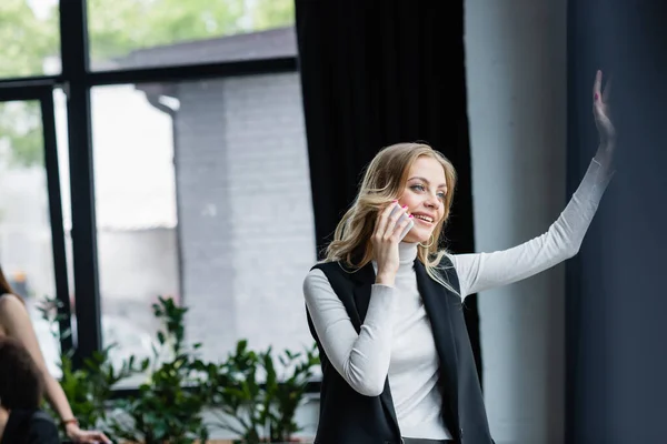 Happy businesswoman talking on smartphone while standing in office — Stock Photo