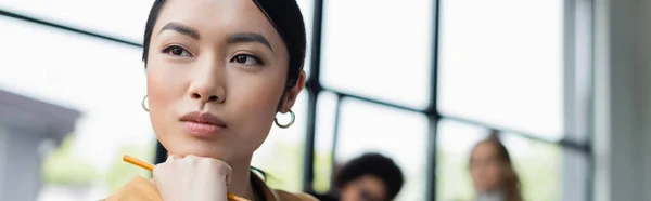 Thoughtful asian businesswoman looking away near colleagues on blurred background, banner — Stock Photo