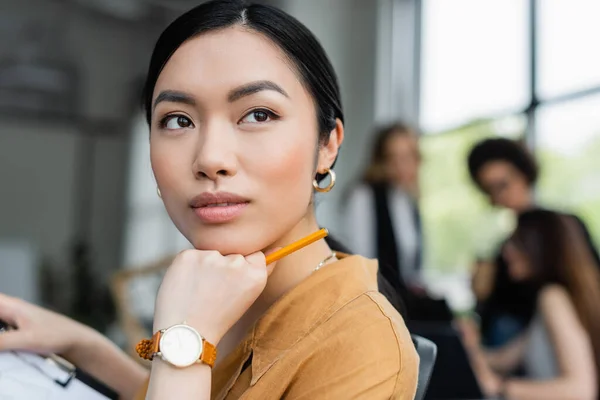 Молодая азиатская бизнесвумен смотрит в сторону, думая в офисе — стоковое фото