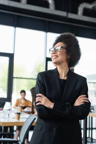 Stylish african american businesswoman smiling while standing with crossed arms — Stock Photo