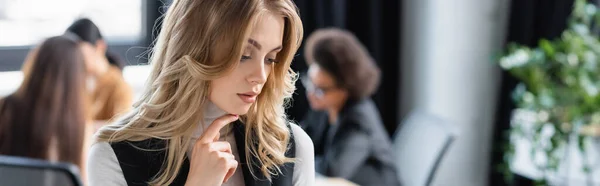 Pensive businesswoman touching chin near multiethnic colleagues on blurred background, banner — Stock Photo