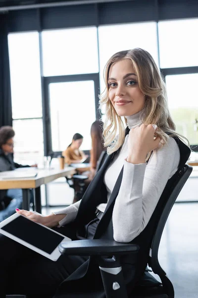 Joven y feliz empresaria sentada en silla de oficina con tableta digital - foto de stock