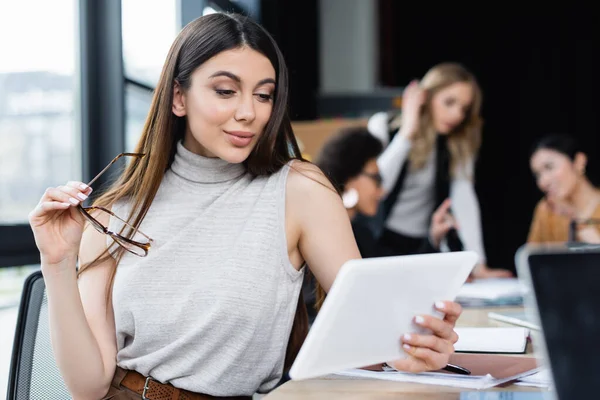 Donna d'affari positiva che tiene il computer portatile e guarda tablet digitale in ufficio — Foto stock