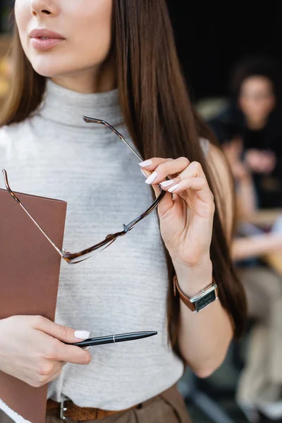 Частичный взгляд предпринимательницы с очками, ручкой и бумажной папкой в офисе — стоковое фото