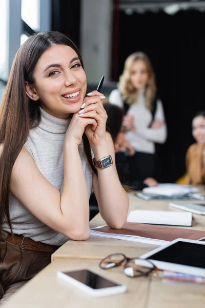 Brunette femme d'affaires souriant à la caméra près de tablette numérique et smartphone avec écran blanc — Photo de stock