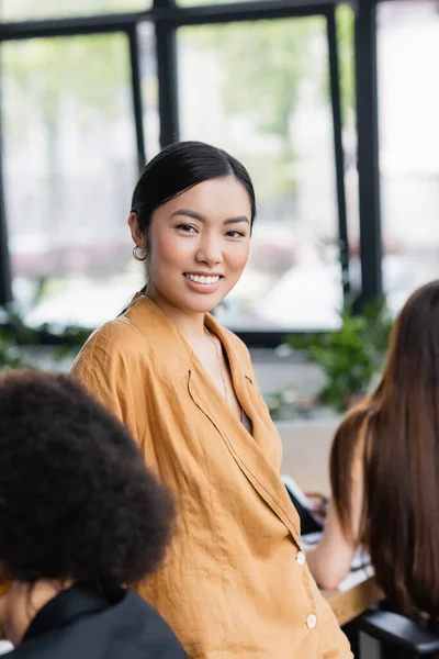 Feliz asiático mujer de negocios sonriendo en cámara cerca borrosa compañeros - foto de stock