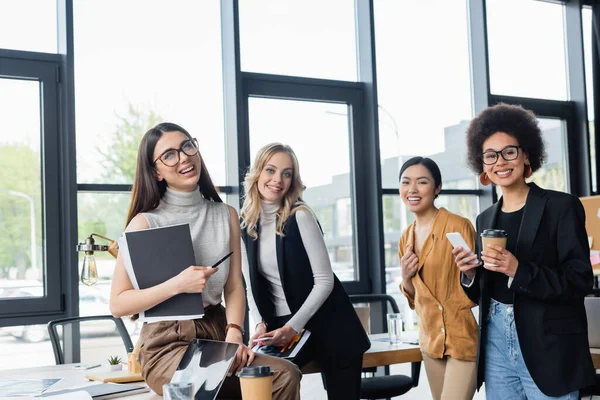 Junge multikulturelle Geschäftsfrauen lächeln während der Kaffeepause im Büro in die Kamera — Stockfoto