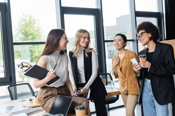 Giovani e felici donne d'affari multietniche che parlano durante la pausa caffè in ufficio — Foto stock