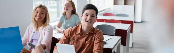 Fröhlicher Schüler mit digitalem Tablet in der Nähe von Klassenkameraden während des Unterrichts, Transparent — Stockfoto