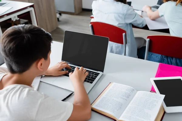 Вид сверху на школьника с помощью ноутбука с чистым экраном возле книги — стоковое фото