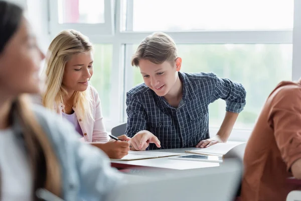 Smiling schoolboy pointing at notebook near friend in classroom — Stock Photo