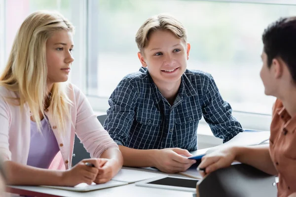 Escolar sonriente mirando a un amigo cerca de portátiles y tabletas digitales - foto de stock