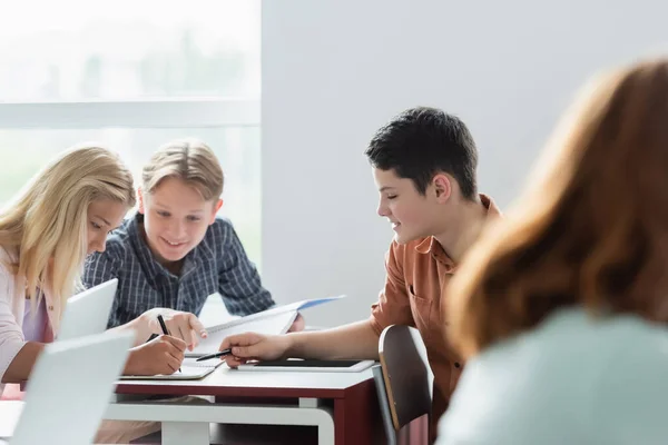 Smiling schoolboys looking at notebook near friend in classroom — Stock Photo