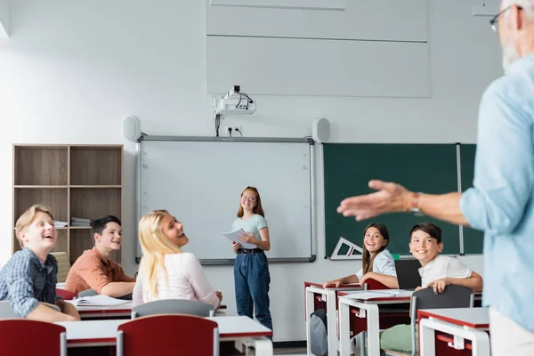 Des élèves multiethniques positifs regardent un enseignant flou — Photo de stock